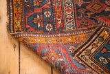 Vintage Malayer rug edge with exposed foundation and tattered ends, displaying geometric patterns.