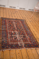 Vintage Malayer rug corner with tattered fringe, exposed foundation, and faded navy Herati pattern.