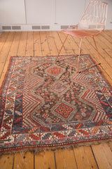 Close-up of vintage Qashqai rug's tattered red and blue bottom right border fringe.