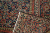 Corner of antique Mahal rug folded, showing intricate Herati pattern, madder red, navy, and light fringe.