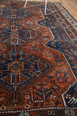 Vintage Qashqai carpet's madder red field with deep blue geometric and plant patterns, showing low pile.