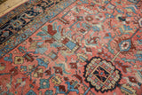 Vibrant geometric floral patterns on a hand-knotted Heriz carpet in blush, sky blue, and wine.