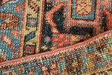 Vintage Heriz carpet's blush edge and hand-knotted geometric patterns in blue, red, beige.