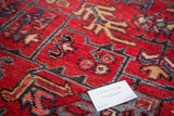 Close-up of vintage Heriz pile featuring geometric leaves and flowers in red, navy, and gold.