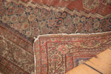 Lifted corner of antique Fereghan rug revealing its red, gold, navy reverse weave and worn edges.