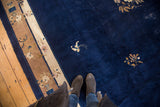 Feet on a late Peking style vintage Chinese rug, with cobalt blue field and floral border.