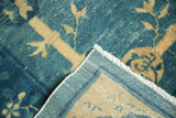 Folded corner of antique Chinese Peking carpet, revealing hand-knotted pile, tight foundation, and white fringe.