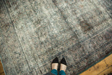 Distressed Persian Meshed carpet showing worn intricate floral motifs, faded blue, and visible foundation.