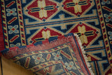 Close-up of hand-knotted Afghan rug's folded corner, showing cherry red, indigo, and saffron geometric pattern.