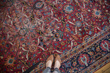 Vintage Persian Yezd carpet: worn red field, blue border, elaborate palmette motifs, person's feet.