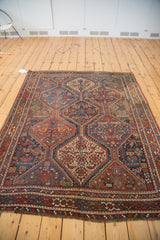 Vintage Qashqai rug corner with madder red border, secured fringe, and animal-filled tribal patterns.