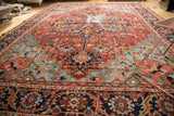 Antique Heriz rug detail: ruby red field, sapphire blue patterns, visible aged wear.