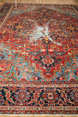 Antique Heriz carpet's intricate navy blue border, ruby red field, and central exposed foundation distress.
