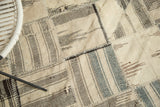 Visible blanket stitching joins ivory, brown, and charcoal geometric Kurdish rug patches.