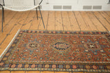 Angled view of a Vintage Karaja rug's dark blue floral border and madder root red field, with mostly even wear.