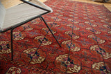 Distressed antique Tekke carpet features repeating gul motifs in brick red, aubergine, and navy.