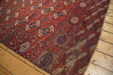 Distressed antique Tekke carpet corner with traditional gul design in brick red, navy, and cream.