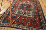 Fringed end of an antique Caucasian rug displaying geometric brick red and blue motifs.