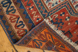 Corner fold of the hand-knotted antique Caucasian rug, revealing brick red pile, ivory fringe, and vibrant orange-blue reverse weave.