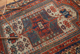 Antique Caucasian rug's geometric prayer mehrab with brick red, teal, sky blue, and ivory patterns.