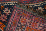 Vintage tribal carpet corner, showing aubergine, navy, and tangerine geometric patterns and worn fringe.