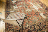 Distressed Mahal carpet with faded brick red floral patterns and navy border, beside a modern chair.