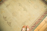 Distressed Indo Chinese carpet, ivory field with subtle scalloped medallions, green-red border, and aged texture.