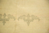 Distressed Indo Chinese carpet detail: ivory field, stylized sage green bat motifs, and soft pile wear.
