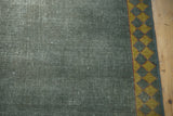 Distressed ocean green rug pile with foundation showing, framed by a saffron diamond border.