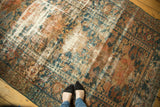 Distressed Hamadan carpet with faded teal, peach, and ivory patterns showing worn texture and knot heads.