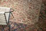 Antique Persian Mahal carpet corner displaying ivory herati field, blush tones, navy border, and worn pile.