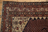 Corner detail of a vintage Malayer rug with white fringe, geometric patterns in cobalt, wine red, and ivory.