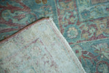 Folded Kerman carpet corner showing faded seafoam green floral pile, visible foundation, and antique ivory backing.