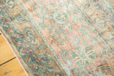 Curvilinear floral motifs on the antique Kerman runner showing muted blush, sea foam green, and ivory hues, with wear.