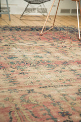 Angled detail of antique Yazd carpet's faded cranberry and ivory floral patterns.