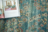 Antique Kerman carpet showing faded teal-blue and plum floral motifs with visible foundation wear.