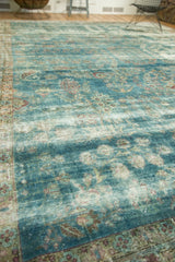 Angled detail of antique Persian Kerman carpet with faded teal, red motifs, and visible foundation.