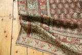 Folded antique Persian Hamadan rug showing worn red boteh, green floral border, and fringe.
