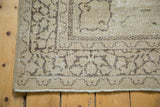 Worn corner of vintage Tabriz rug with faded charcoal trefoil motifs and ivory fringe.