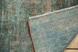 Folded corner of vintage Lilihan carpet, showing faded green, teal, and blush pile and woven foundation.