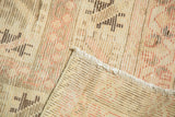 Folded corner of vintage Oushak carpet showing worn pile, woven back, and secured side selvage.
