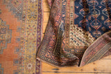 Folded vintage Kurdish rug revealing geometric borders in navy, blush, and brown.