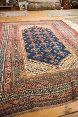 Kurdish rug corner detail: geometric borders, navy field, blush germinating plant motifs, and fringe.