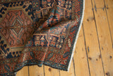Folded vintage Karaja rug shows geometric navy, red, gold, green patterns, dark selvage, and fringe.