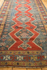 Angled view of Antique Kazak rug's geometric diamond medallions, red and teal blue patterns, and textured wear.