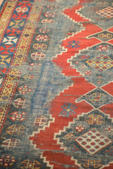 Geometric red and blue patterns dominate this antique Kazak runner, revealing its worn foundation.