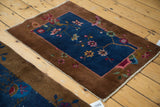 Corner of an antique Fette Li rug with brown border, navy field, and art deco floral motifs.