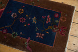 Angled detail of hand-knotted Fette Li rug: navy Art Deco florals, copper border, fringe.