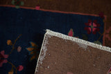 Detailed corner of an antique Fette Li rug, showing hand-knotted brown foundation, white fringe, and navy blue floral pile.