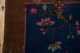 Intricate blush and dusty gold stylized florals on navy field of antique Fette Li rug, brown border.